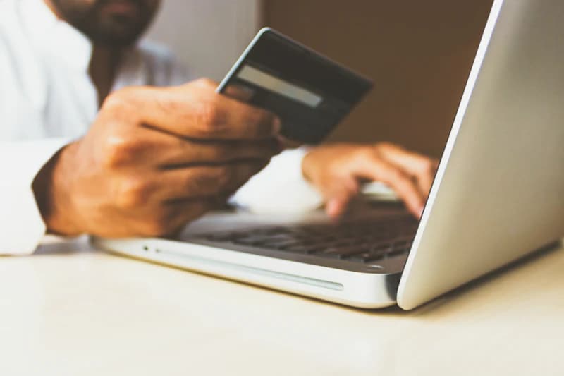 Hands holding a bank card while paying on a laptop